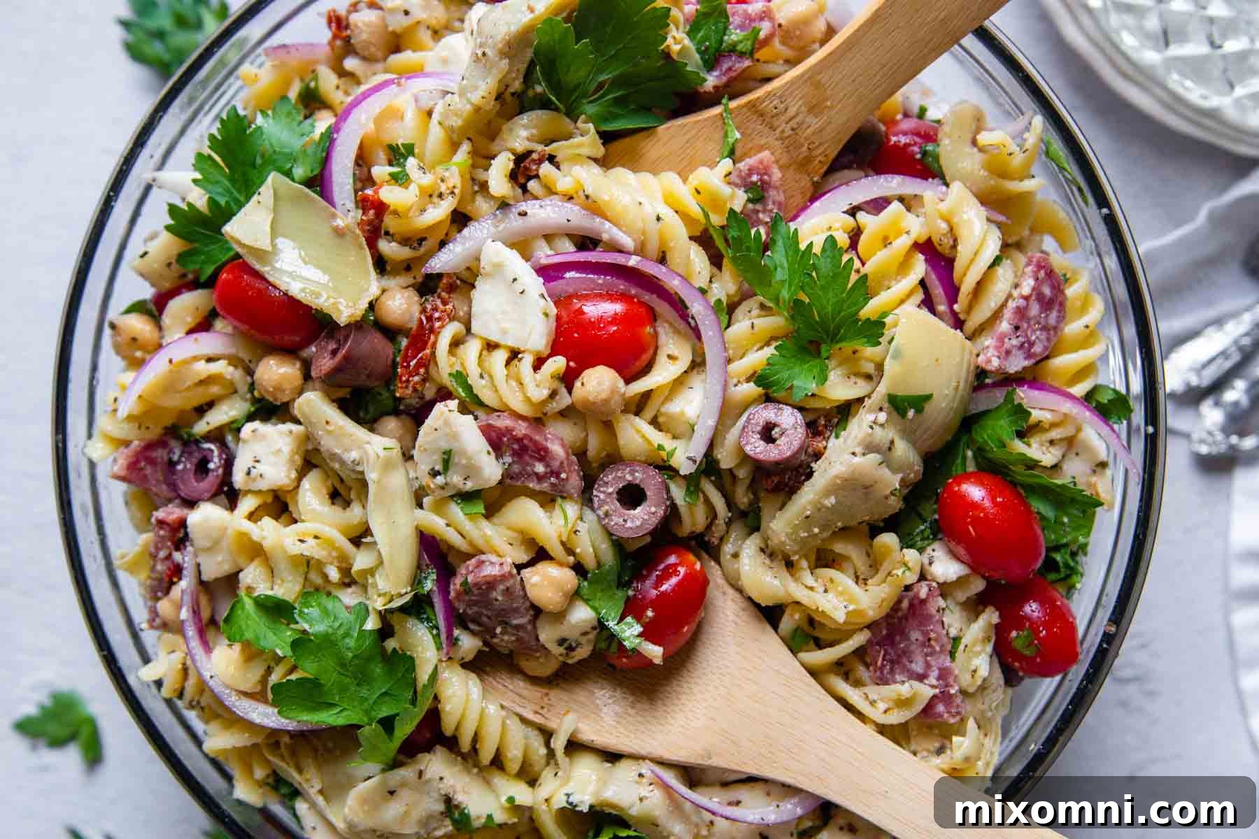 An overhead shot of a prepared gluten-free pasta salad in a glass bowl, with wooden serving spoons, highlighting its inviting and customizable nature.