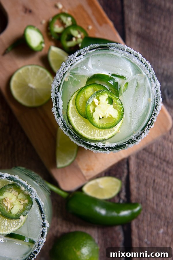 A close-up top view of a spicy margarita, garnished with fresh jalapeño slices and lime wedges, ready to be enjoyed.
