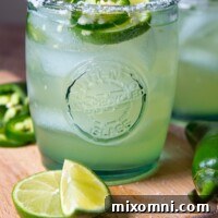 a margarita on a wooden cutting board with fresh jalapenoes and limes around it