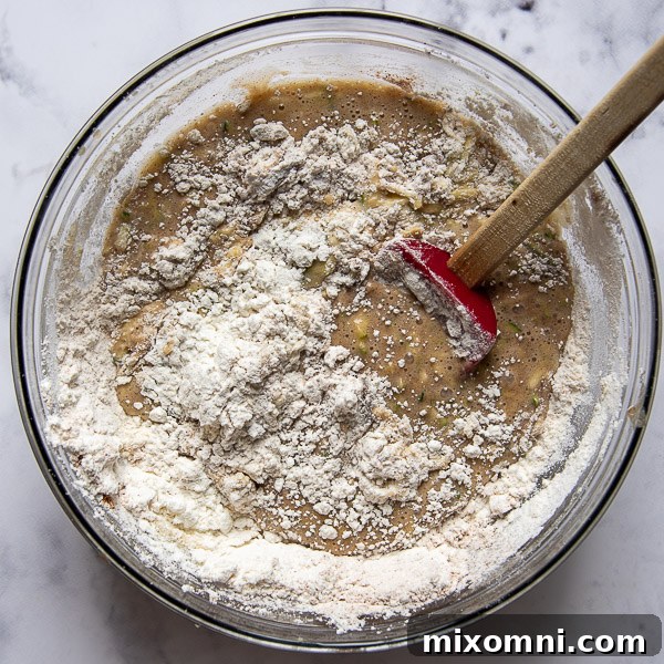 Gluten-free flour being gently stirred into the zucchini bread batter, creating a smooth and consistent mixture.