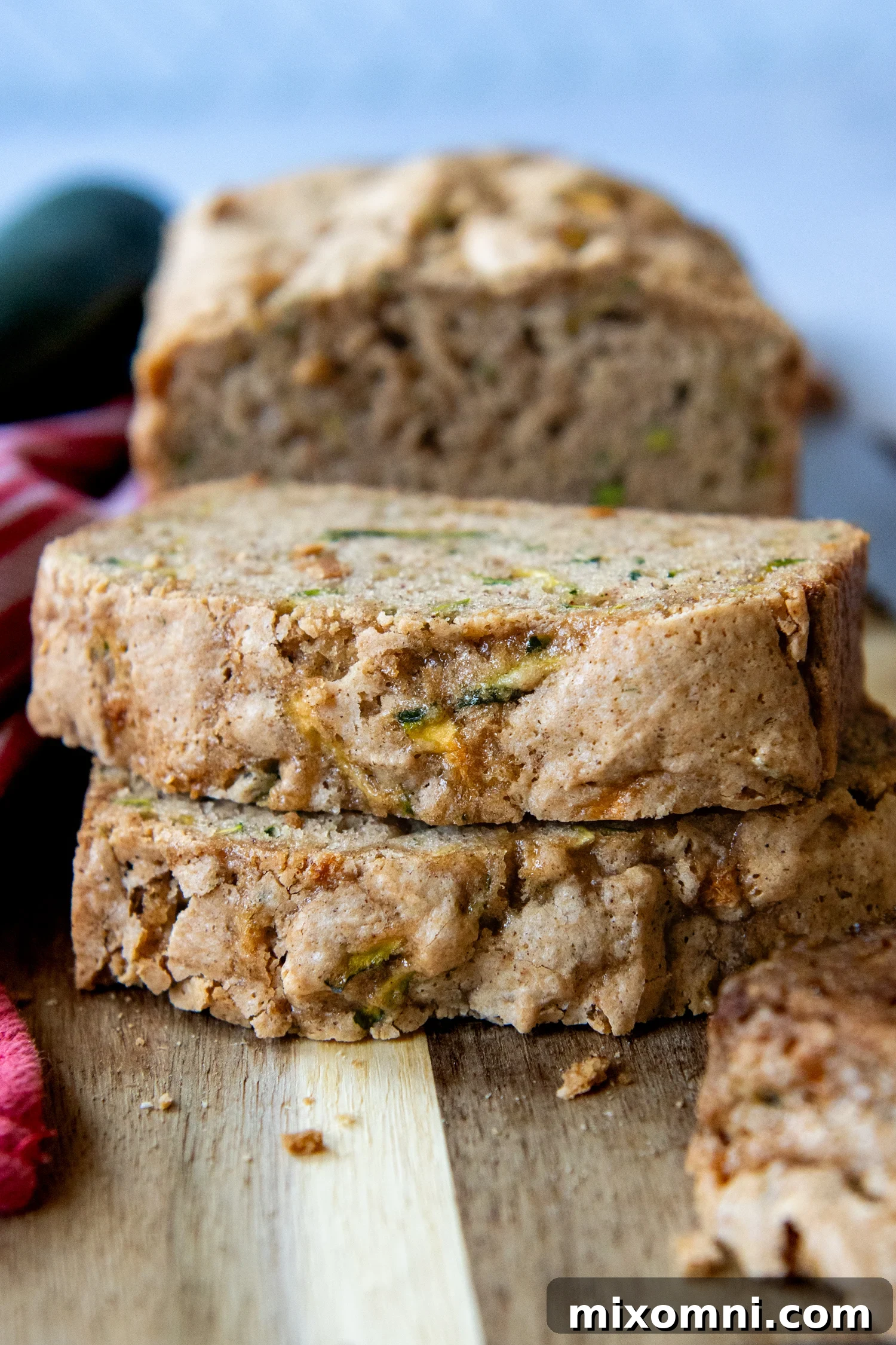 Two generous slices of homemade gluten-free zucchini bread stacked appealingly on a wooden cutting board, revealing a tender, speckled interior.