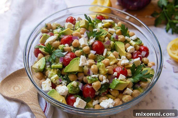 A large serving bowl of Mediterranean chickpea avocado salad with a wooden serving utensil resting next to it.