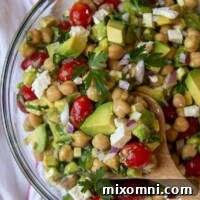 A wooden spoon holding up a serving of chickpea avocado salad