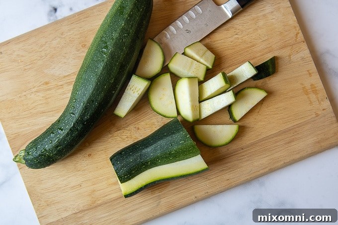 Fresh zucchini being sliced into uniform semi-circles on a wooden cutting board with a sharp knife, ready for sauteing.