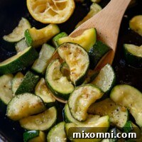 Close up shot of cooked zucchini and squash held by a wooden spoon, ready to be served.