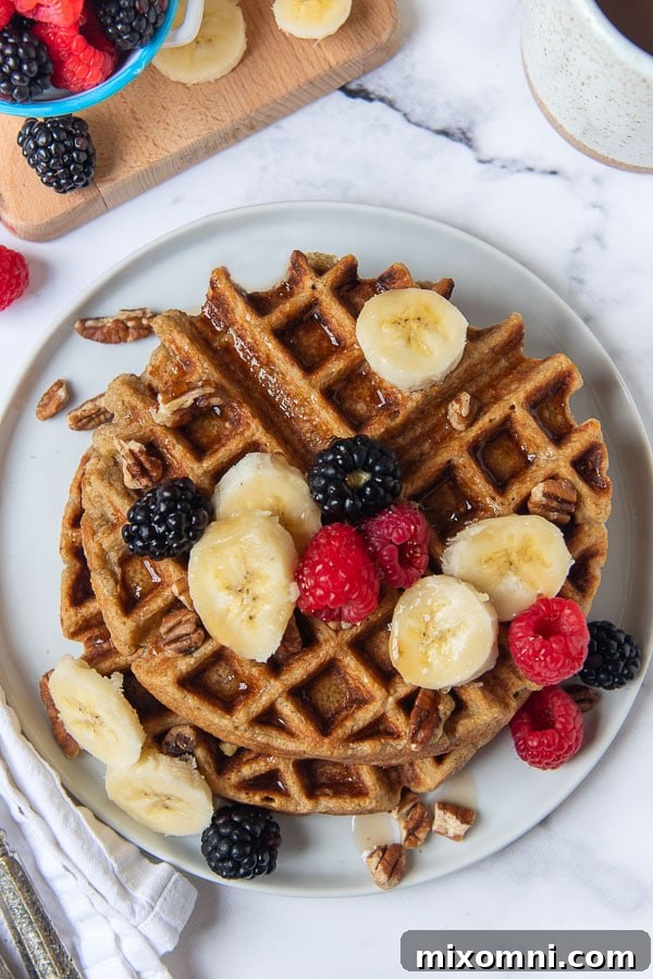 A beautiful overhead shot of golden brown gluten-free banana oatmeal waffles artfully arranged on a white plate.