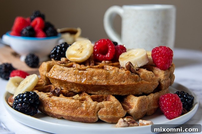 A close-up shot of a stack of two fluffy gluten-free banana waffles, beautifully garnished with sliced bananas and fresh berries.