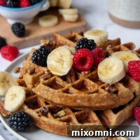 shot of gluten free waffles on a plate with berries, nuts, and bananas on top