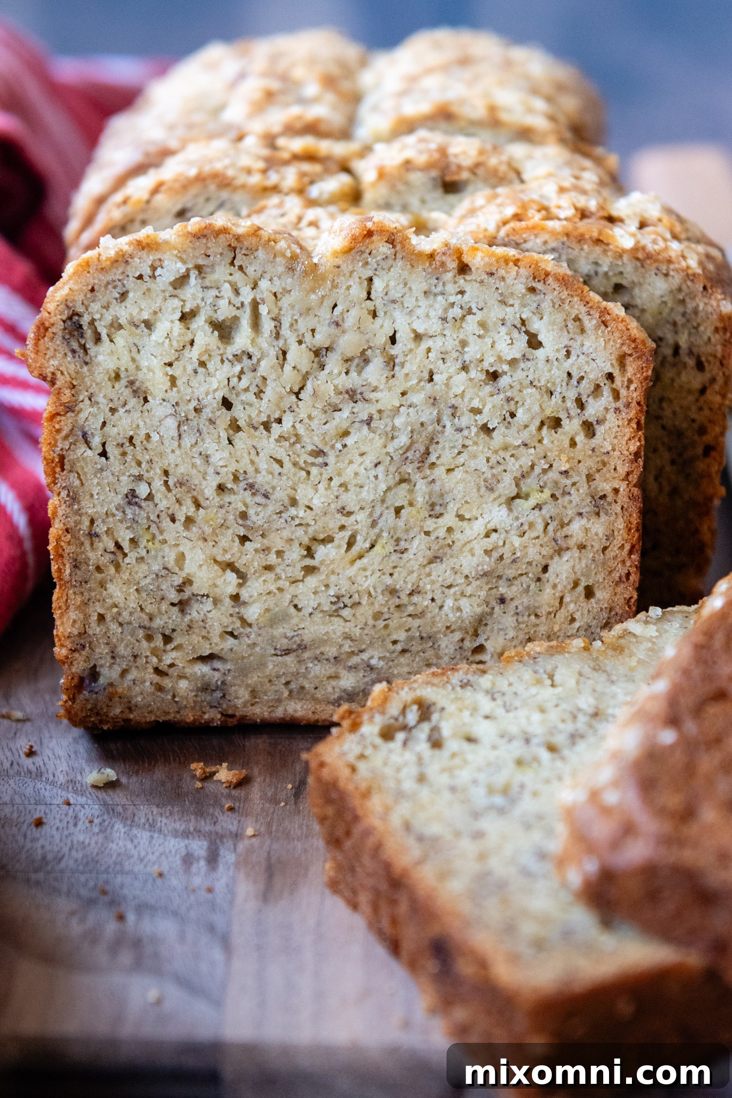 A perfectly baked, sliced gluten-free banana bread loaf, cut open to reveal its moist and tender interior, positioned invitingly towards the camera on a wooden surface.