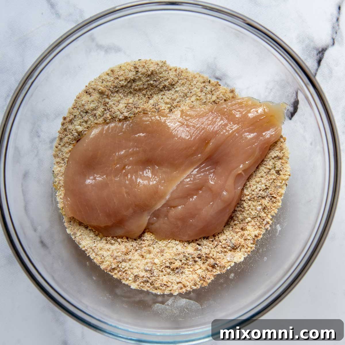 raw chicken breast in a bowl of seasoned breadcrumbs.