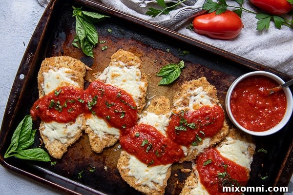 overhead shot of a baking sheet of gluten free chicken parmesan with fresh basil scattered around and a cup of marinara