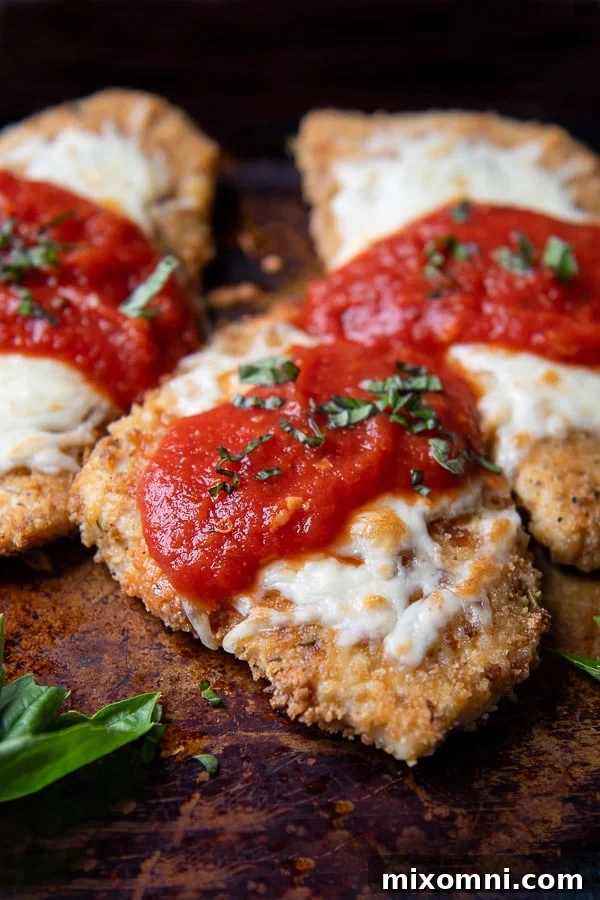 a close up of parmesan chicken on a baking sheet with sauce and cheese on top