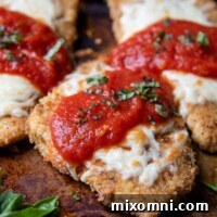 a close up of parmesan chicken on a baking sheet with sauce and cheese on top