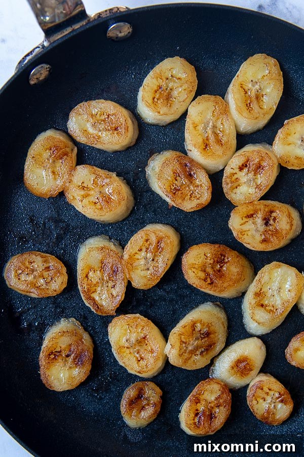 Overhead shot of golden brown pan-fried banana slices arranged in a saute pan, ready to be used as a delicious topping for the banoffee cake.