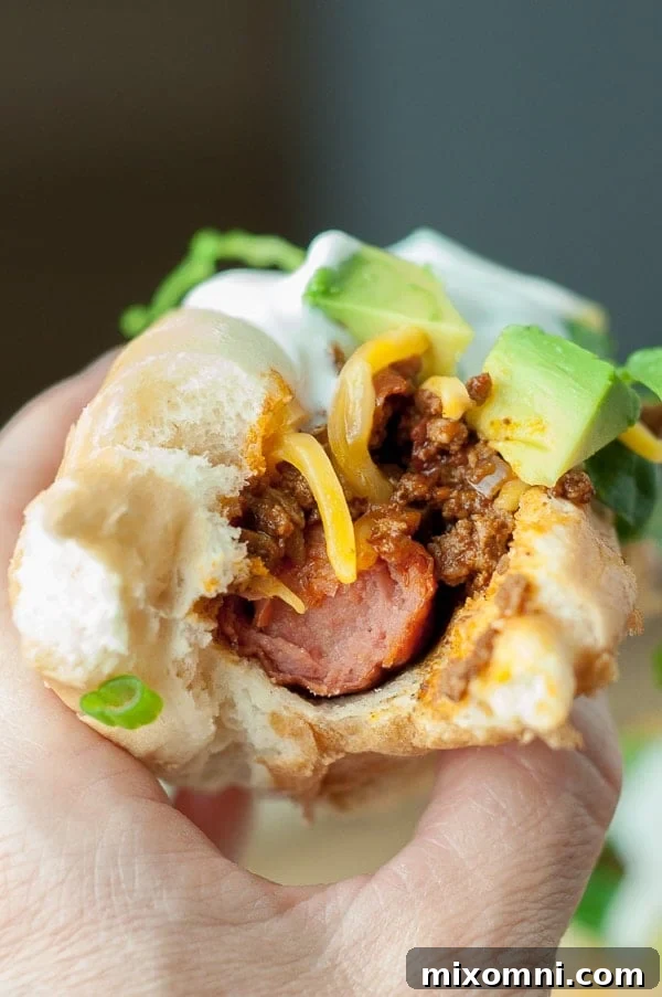 A hand holding a delicious Mexican-style hot dog with a bite taken out, showcasing the generous toppings.