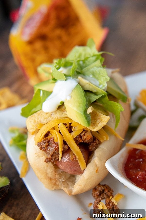 A fully assembled Mexican hot dog on a plate, highlighting the rich ground beef topping and vibrant fresh ingredients, with a small dish of salsa on the side.