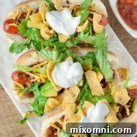 An overhead shot of Mexican hot dogs on a white rectangle plate with a small dish of salsa next to it