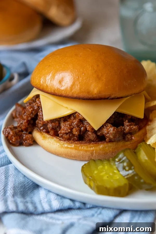 A close-up of instant pot sloppy joes on a white plate with two slices of cheese melting over the meat, served on a toasted bun.