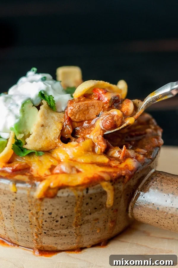 A close-up of a spoon scooping a bite of chicken chorizo chili topped with melted cheese, ready to be enjoyed.