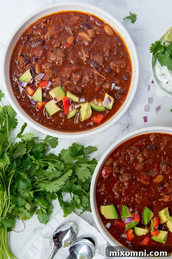 An overhead shot of two inviting bowls of chicken chorizo chili, garnished generously with fresh avocado slices.