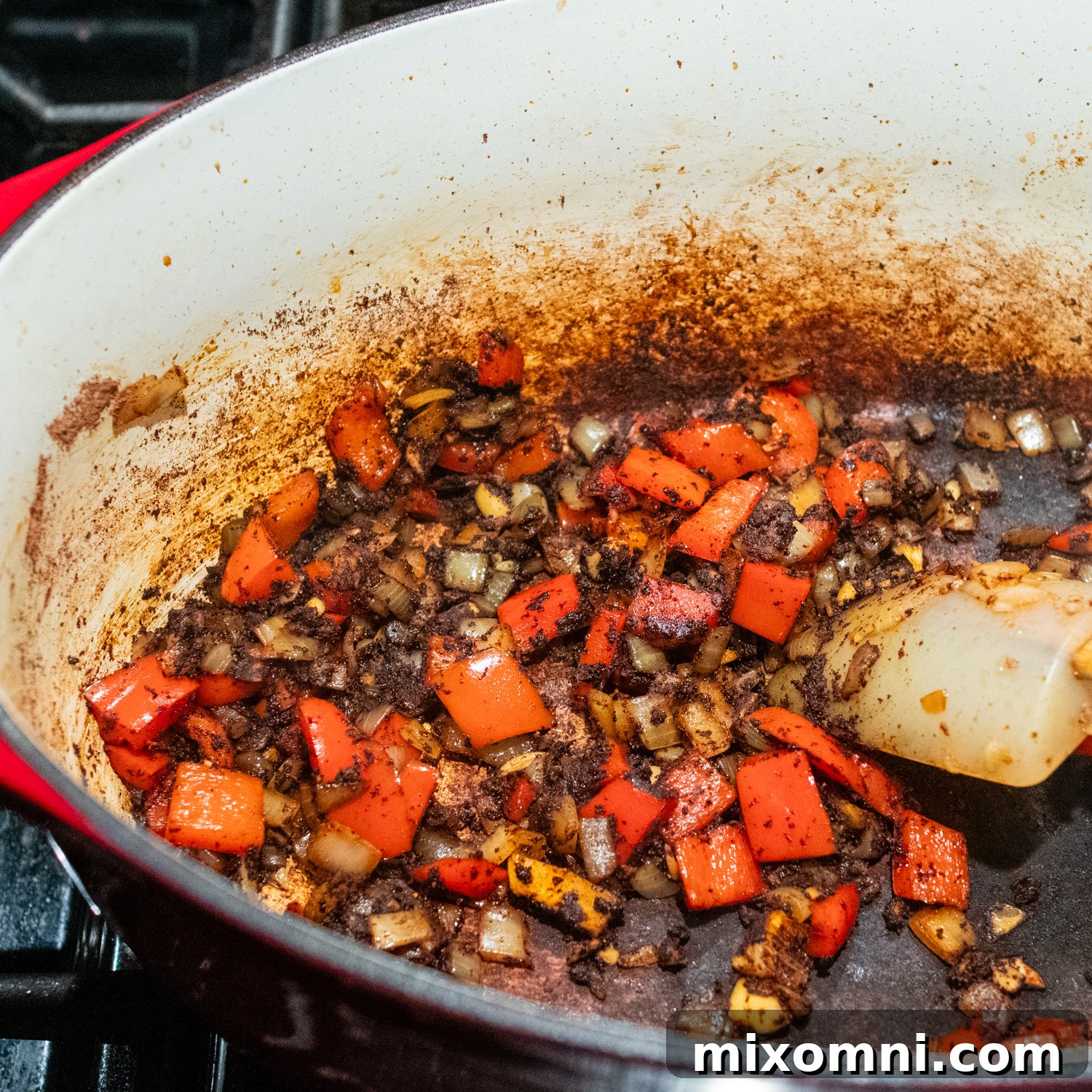 Chopped peppers, onions, and spices being added to a pot with chorizo drippings.