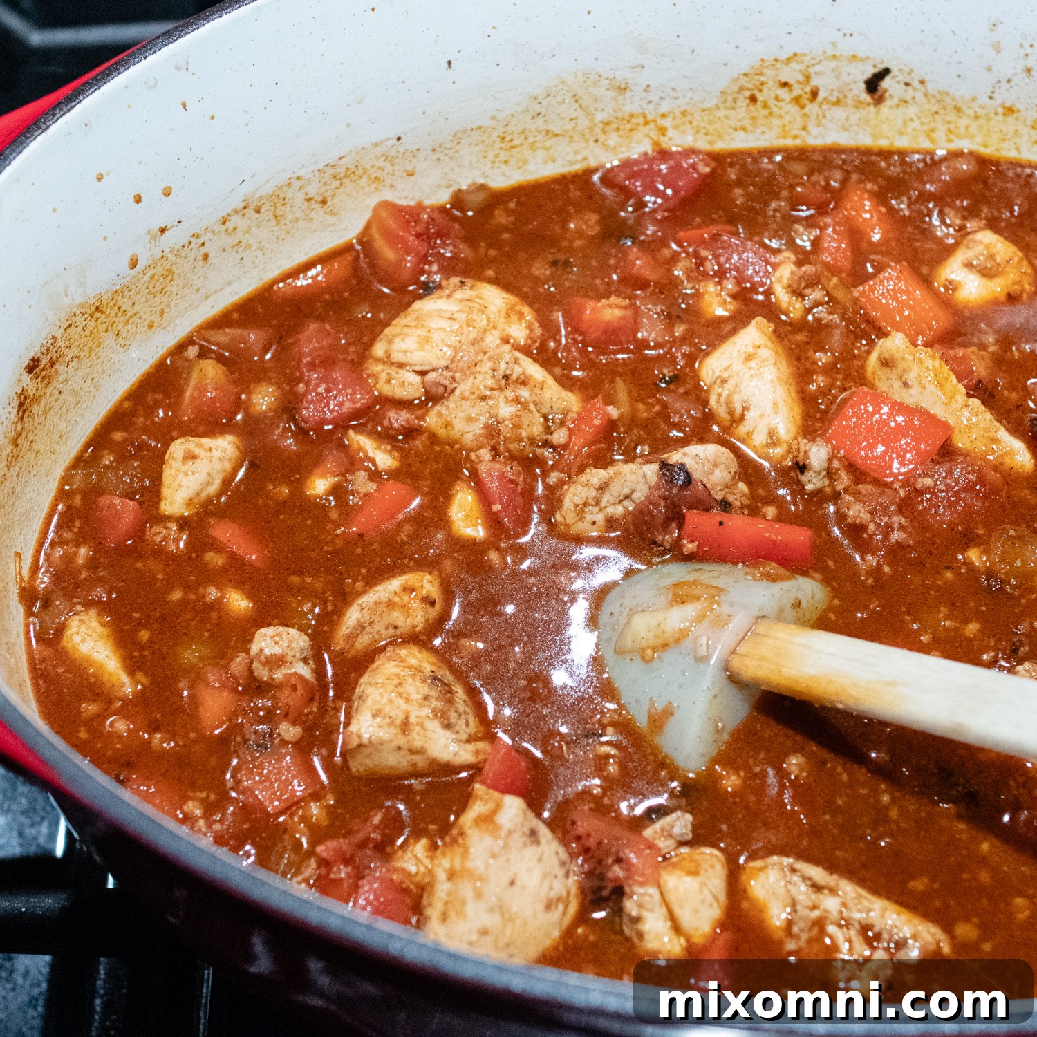 The rich red sauce being poured over chicken in a pot, ready for simmering.