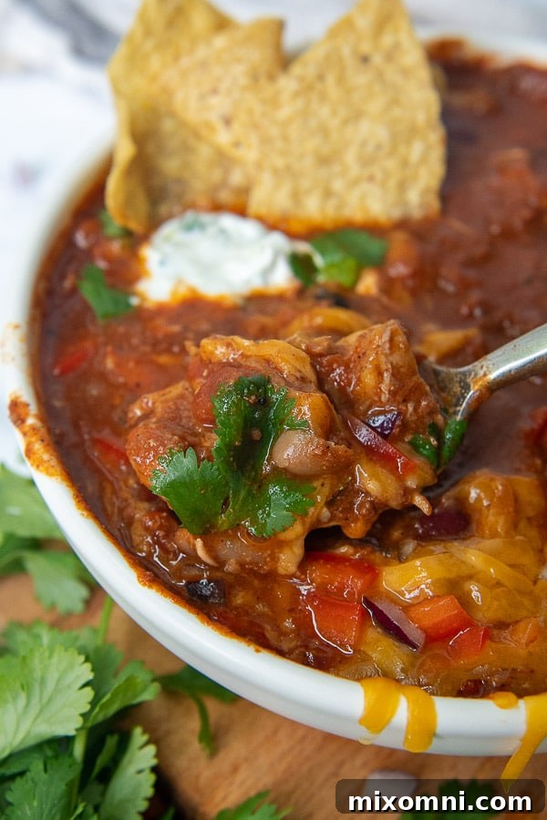 A spoon diving into a rich bowl of chicken and chorizo chili, steam rising from its depths.