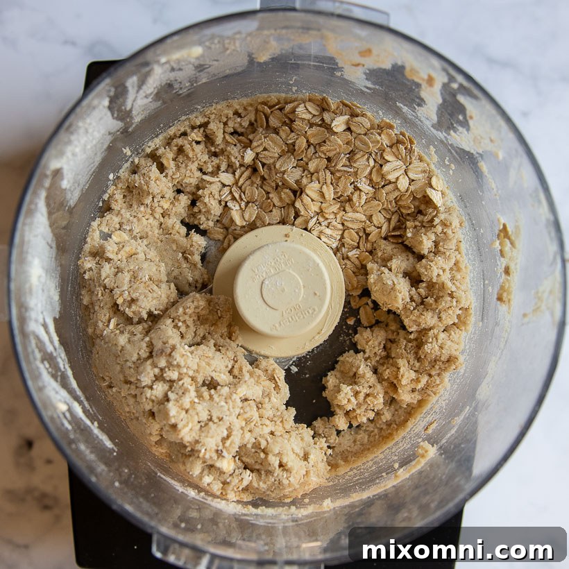 An overhead view inside a food processor shows the thoroughly mixed oat topping, now cohesive and crumbly, forming perfect clusters.