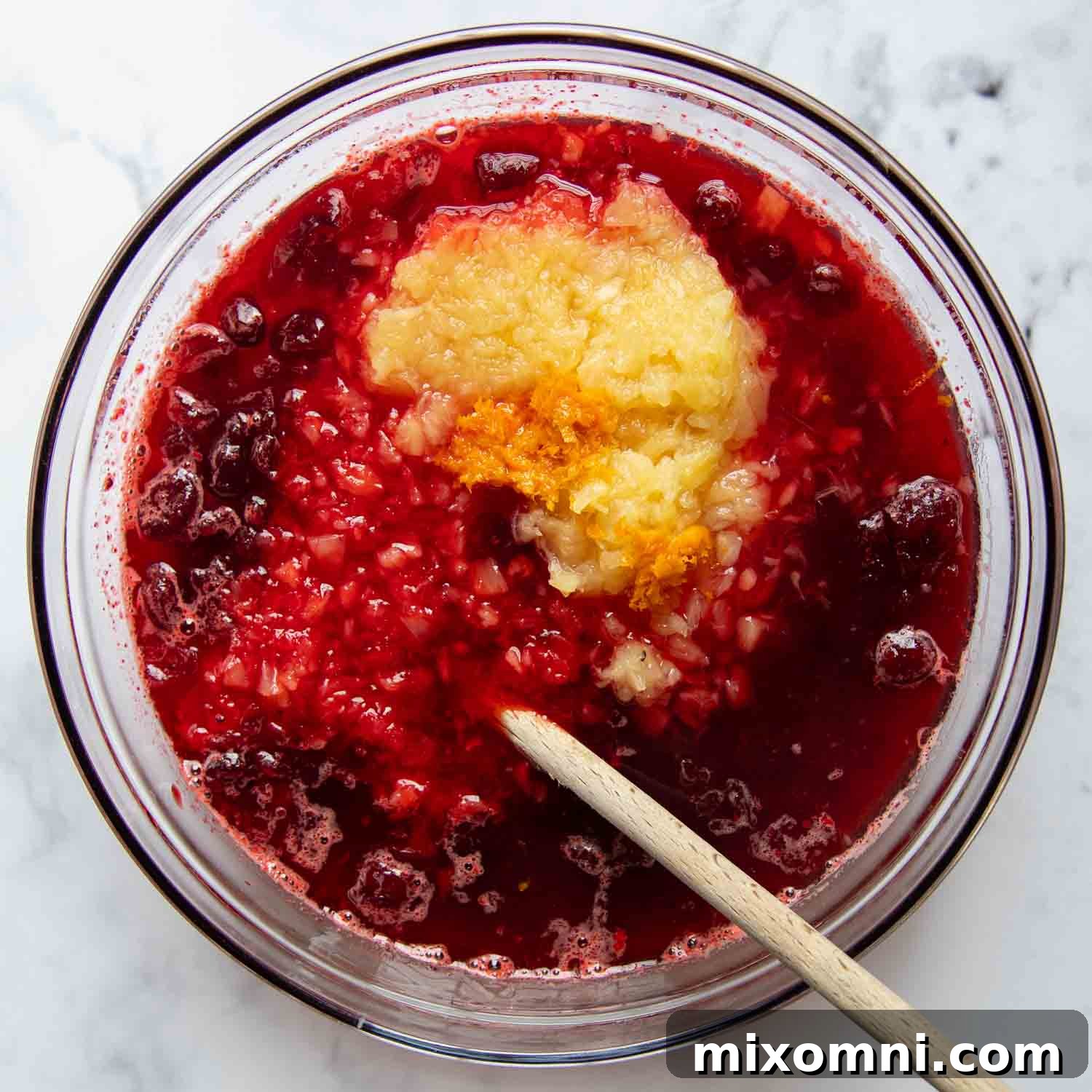 Dissolved jello with cranberry sauce and crushed pineapple mixed in a large glass bowl, ready for chilling.