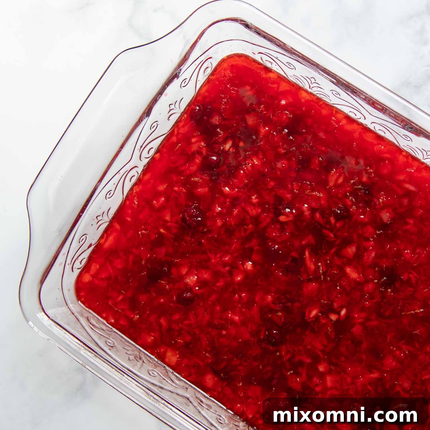 A glass dish filled with cranberry jello, chilling in the refrigerator.