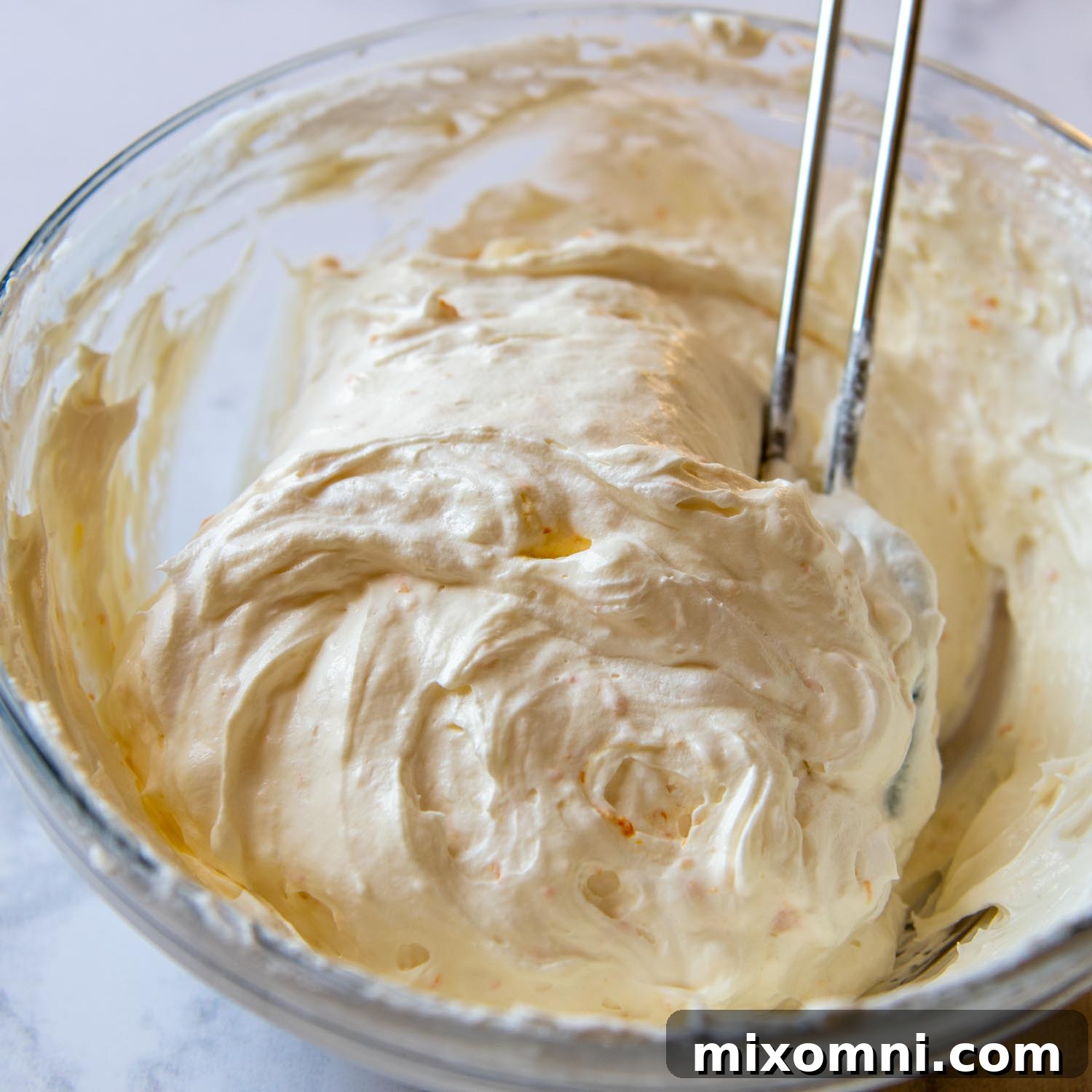 Creamy whipped topping with orange zest in a large glass bowl, ready to be spread.