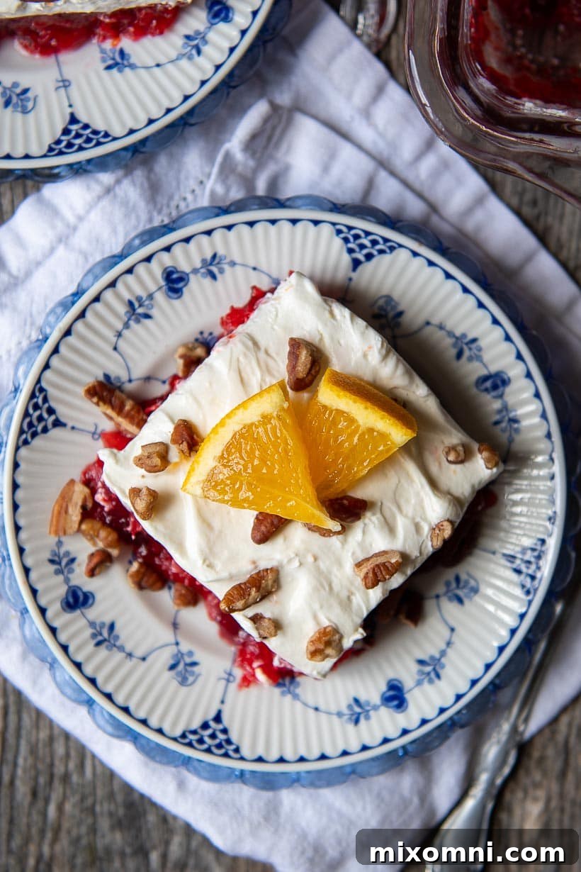 Overhead shot of a perfect slice of cranberry jello salad on a plate, garnished with nuts and an orange slice.