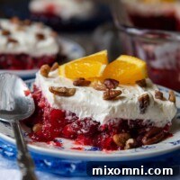 A slice of cranberry raspberry jello salad on a plate with a spoon, showing a bite taken out.