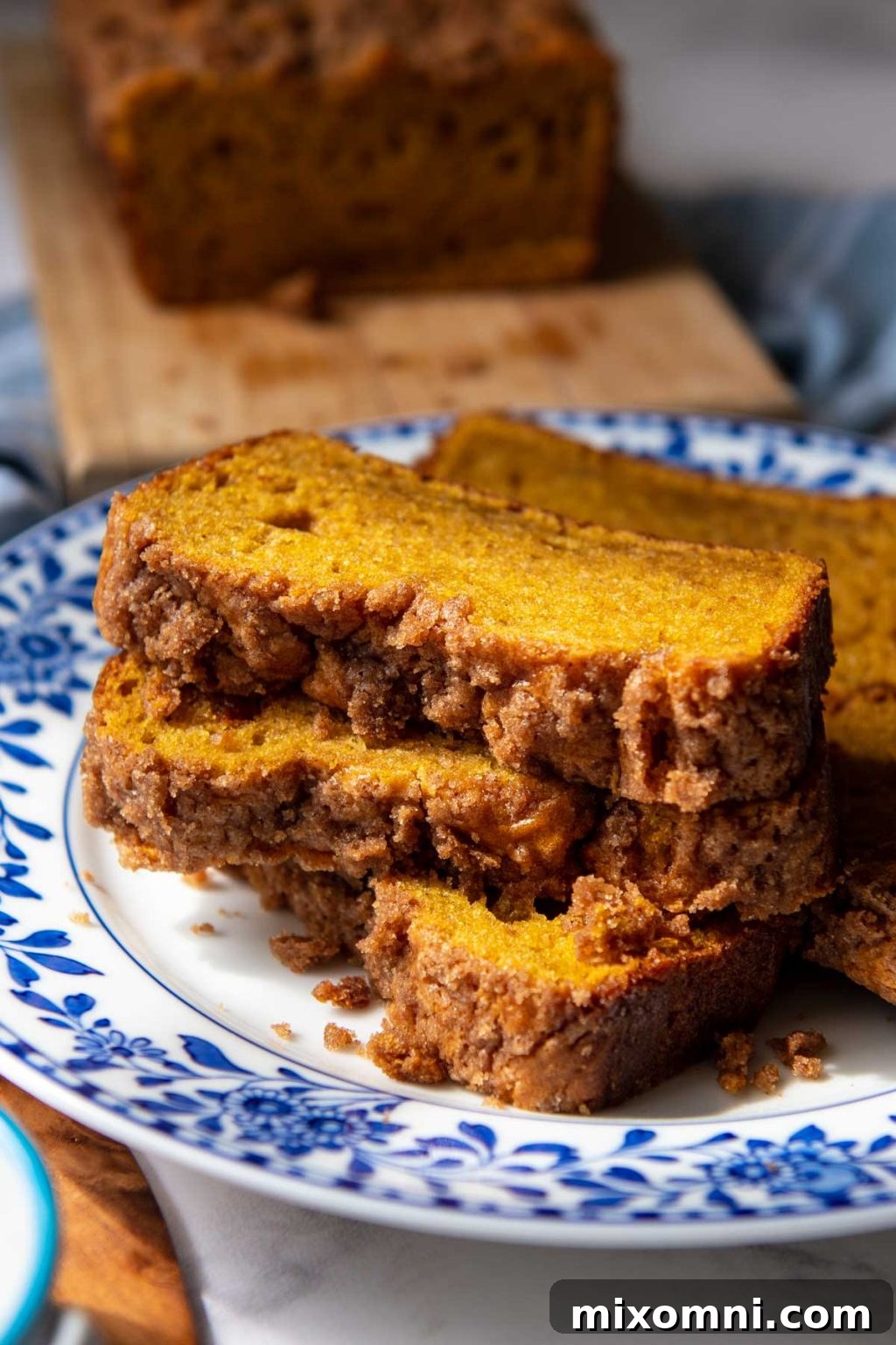 Stacked slices of ultra moist gluten-free pumpkin bread with a delightful streusel topping, presented on a charming blue and white floral plate.