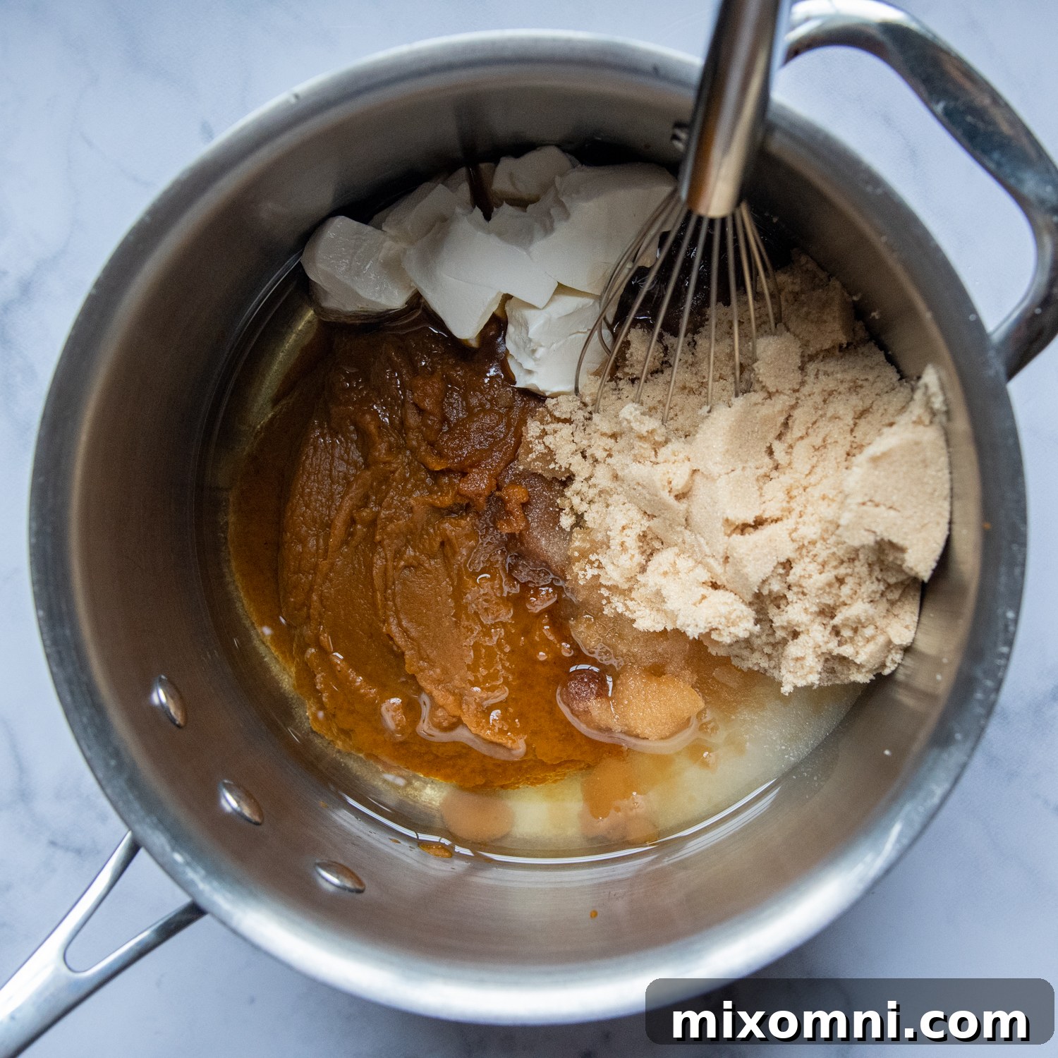 Granulated sugar, brown sugar, and cream cheese being whisked into the cooked pumpkin mixture in a saucepan.