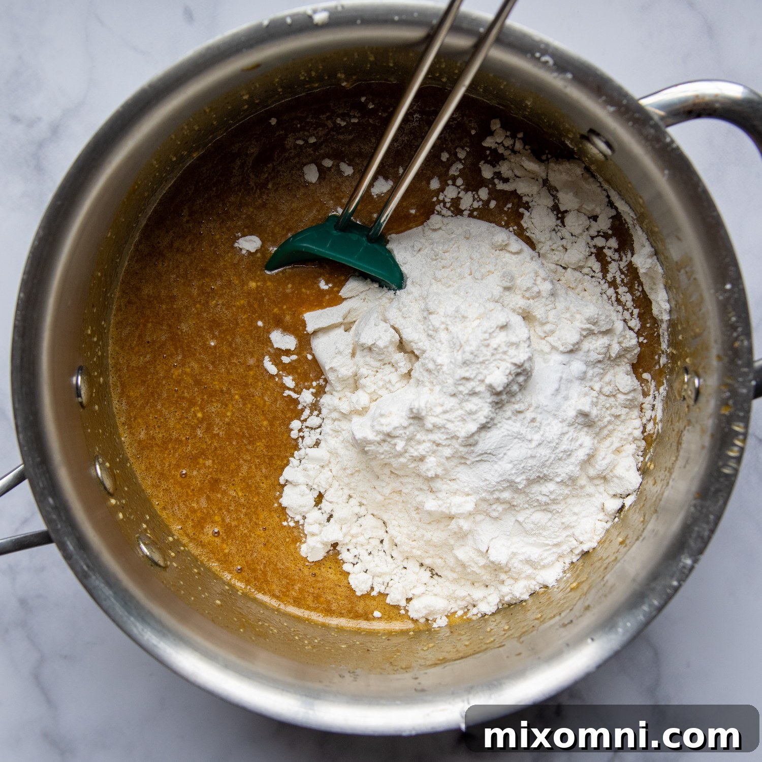 The process of stirring gluten-free flour, baking powder, and baking soda into the pumpkin mixture in a saucepan.