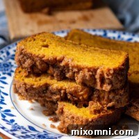 A stack of three slices of gluten-free pumpkin bread with streusel topping on a blue and white flower plate, showcasing its moist texture.