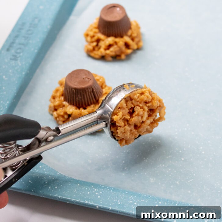 A medium cookie scoop portioning out the crispy rice cookie base onto a baking sheet, illustrating the assembly process.