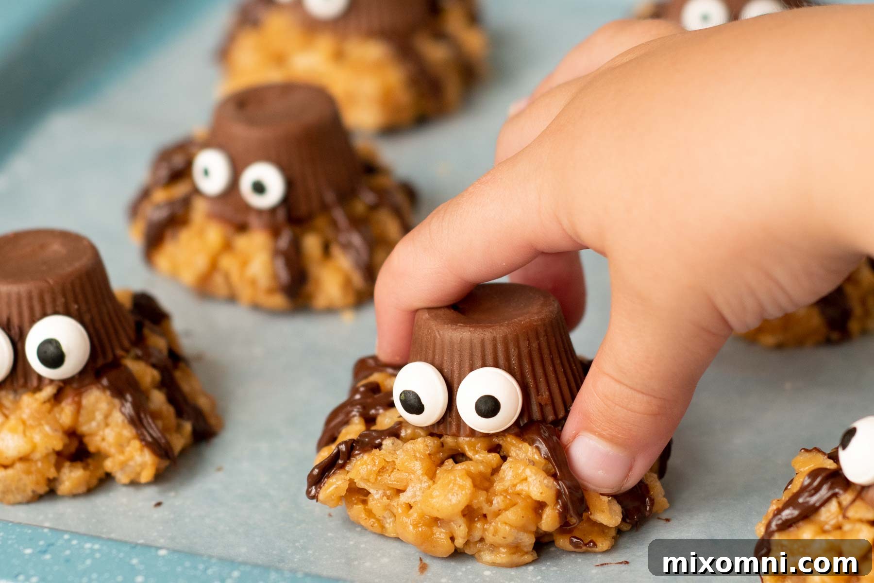 A child's hand reaching for a finished, decorated spider cookie from a plate, highlighting the fun and appeal to kids.