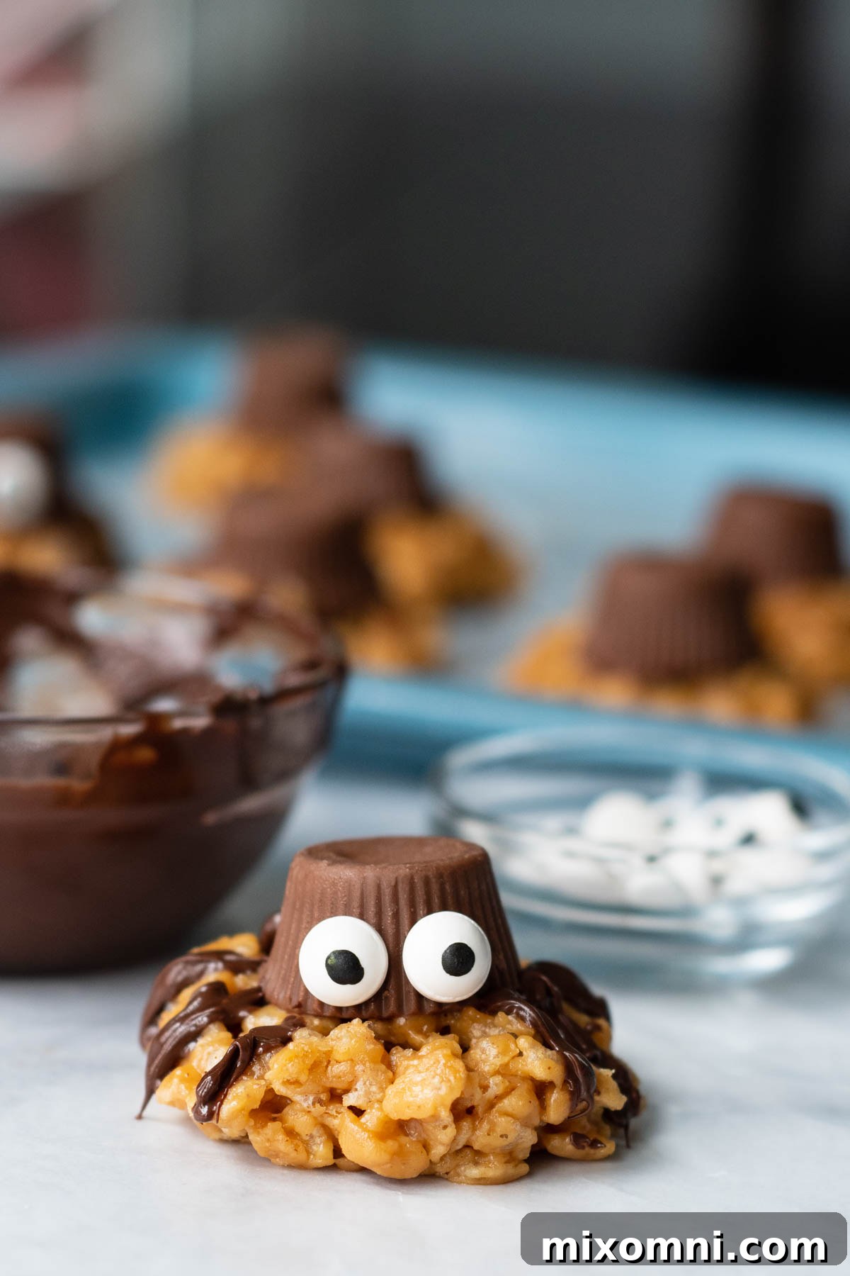 A detailed close-up of a single no-bake spider cookie facing the camera, with more cookies visible on a baking sheet in the soft-focused background.