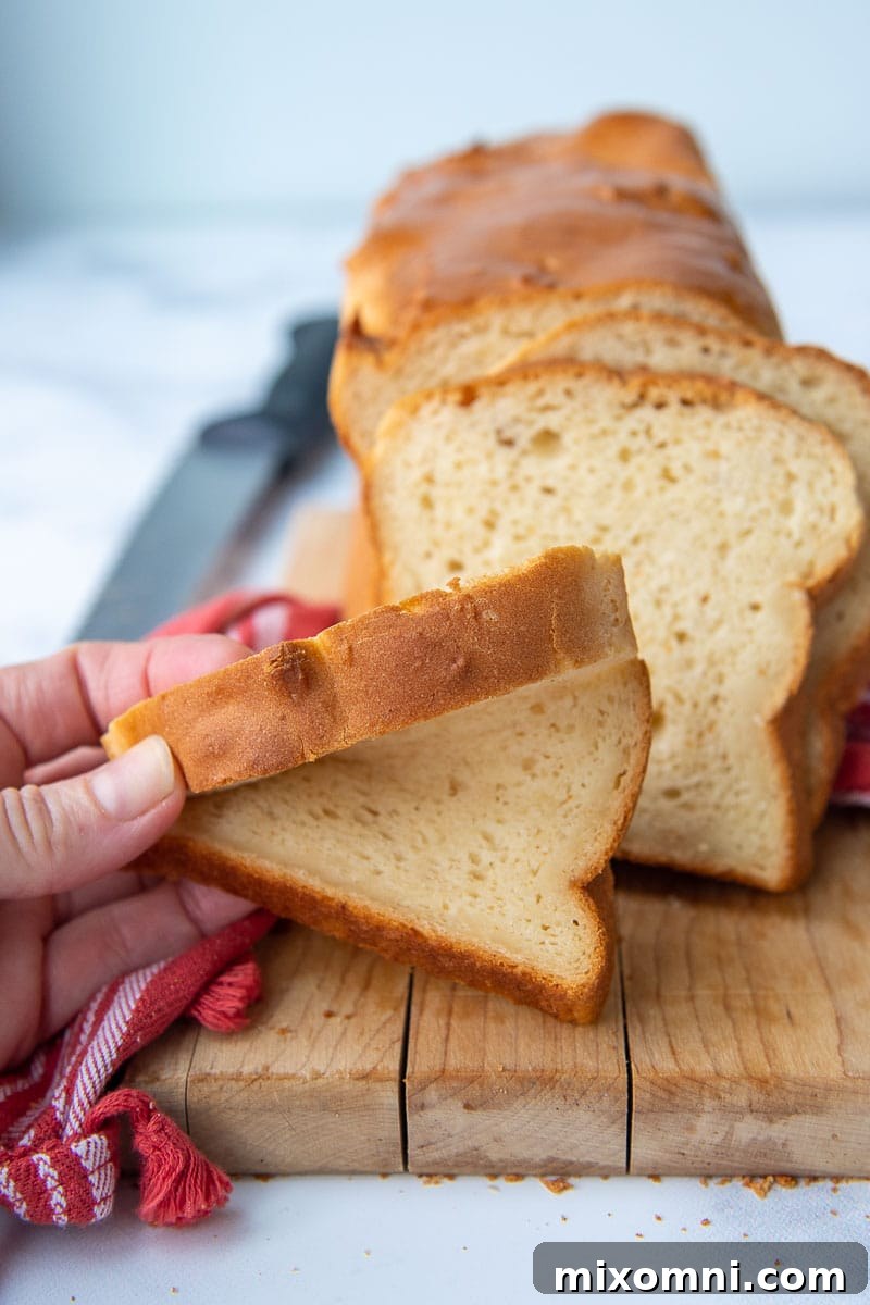 A hand gently squishing a slice of freshly baked gluten-free bread, demonstrating its remarkable softness and squishiness.