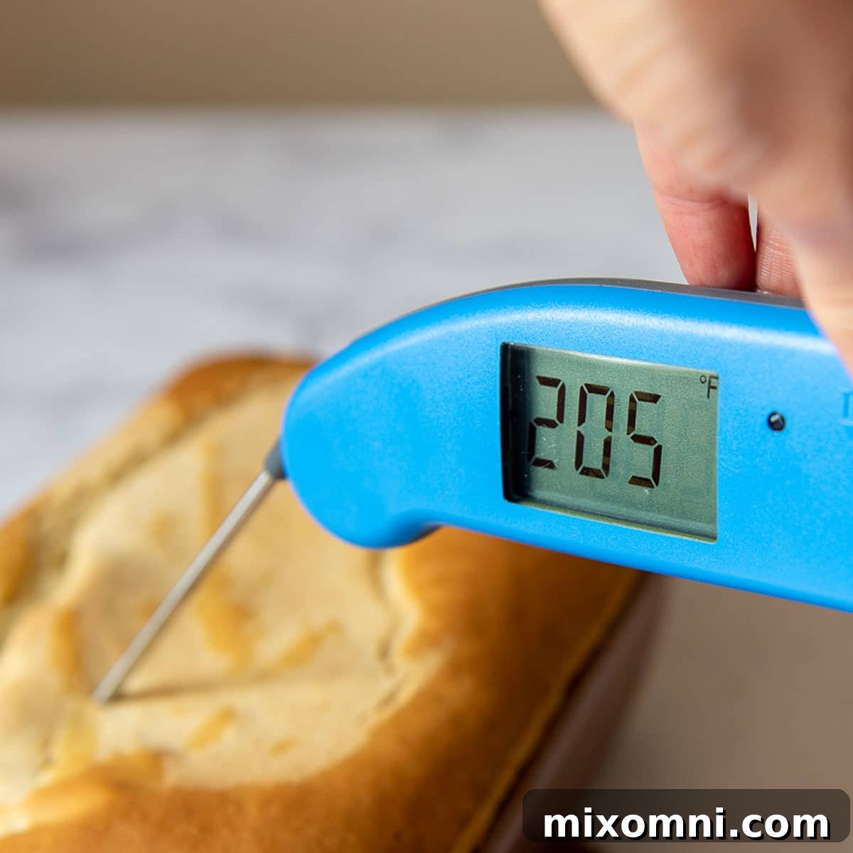An instant-read thermometer being inserted into a freshly baked loaf of gluten-free bread to check its internal temperature.