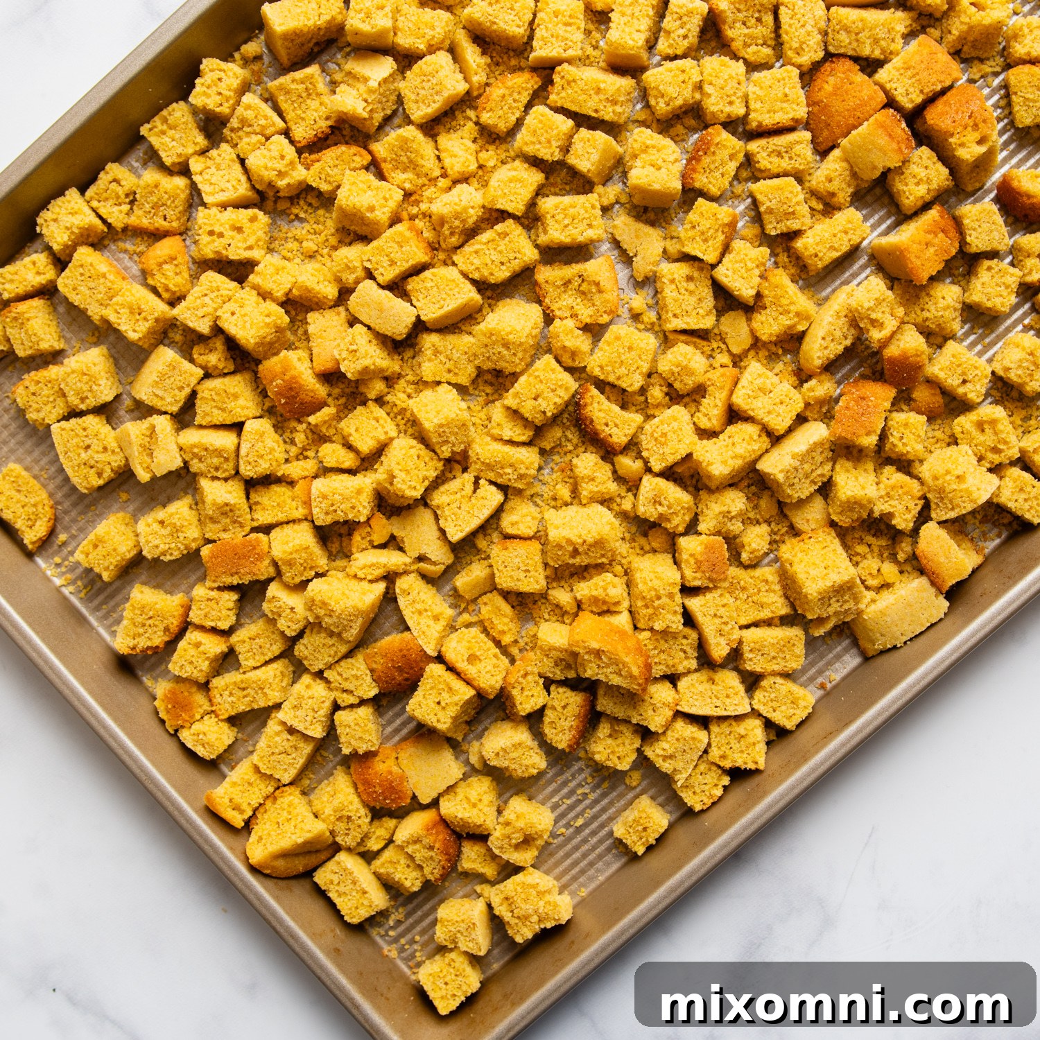 Gluten-free cornbread cubes drying on a baking sheet, ready for stuffing preparation.