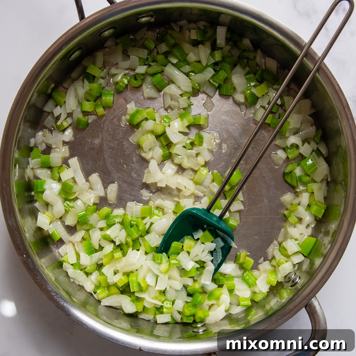 Chopped celery and onion gently cooking in melted butter in a skillet, softening to create the aromatic base for the stuffing.