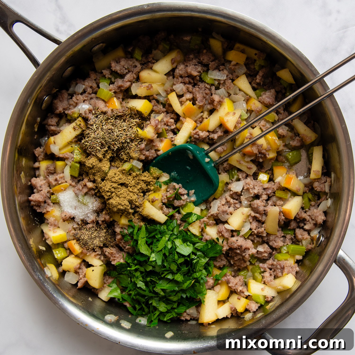 A savory mixture of browned sausage, sautéed apples, vegetables, and aromatic herbs cooking in a skillet, ready to be combined with cornbread.