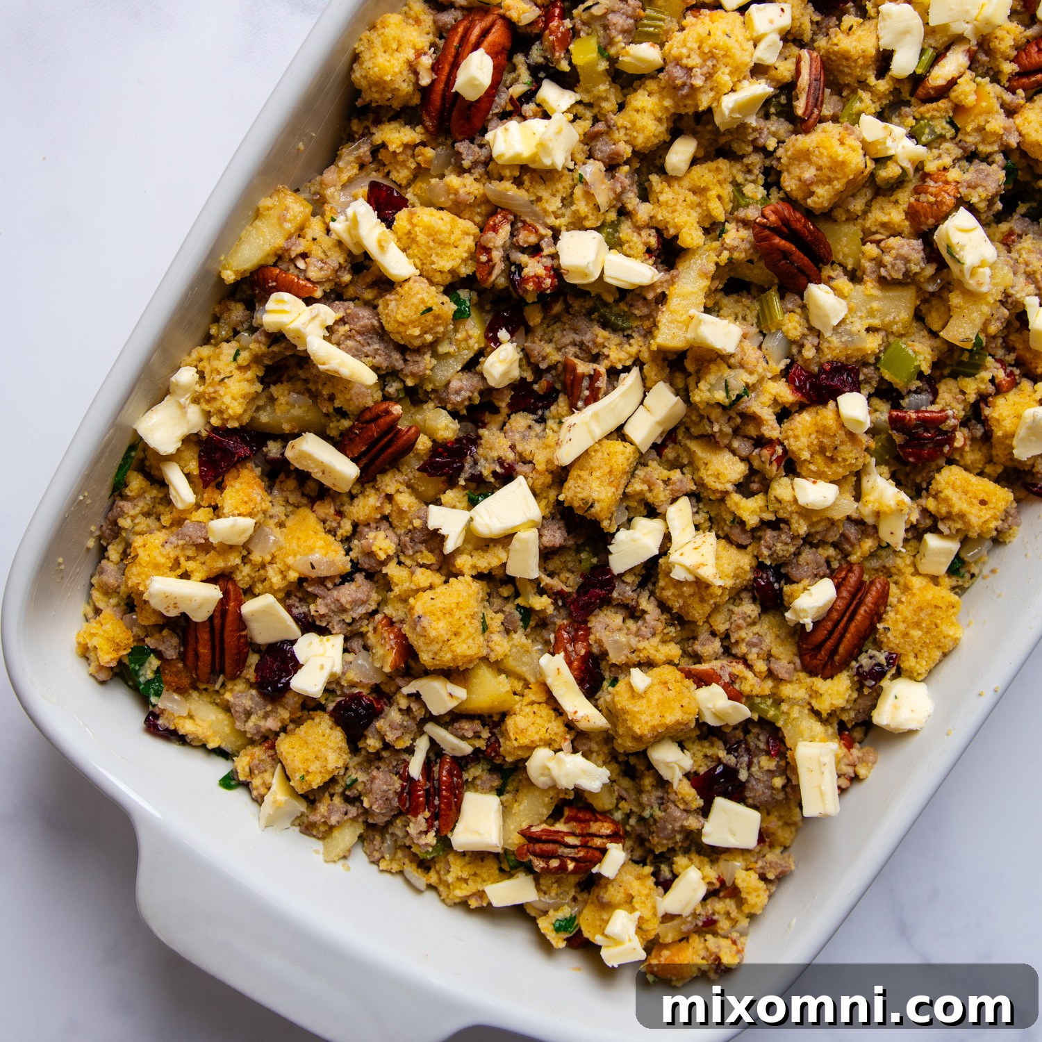 Gluten-free cornbread stuffing spread evenly in a casserole dish, topped with diced butter, ready to be baked to a golden perfection.