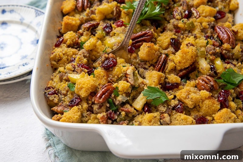 A close-up of golden-brown gluten-free cornbread stuffing in a white baking dish, with a serving spoon poised to scoop a portion.