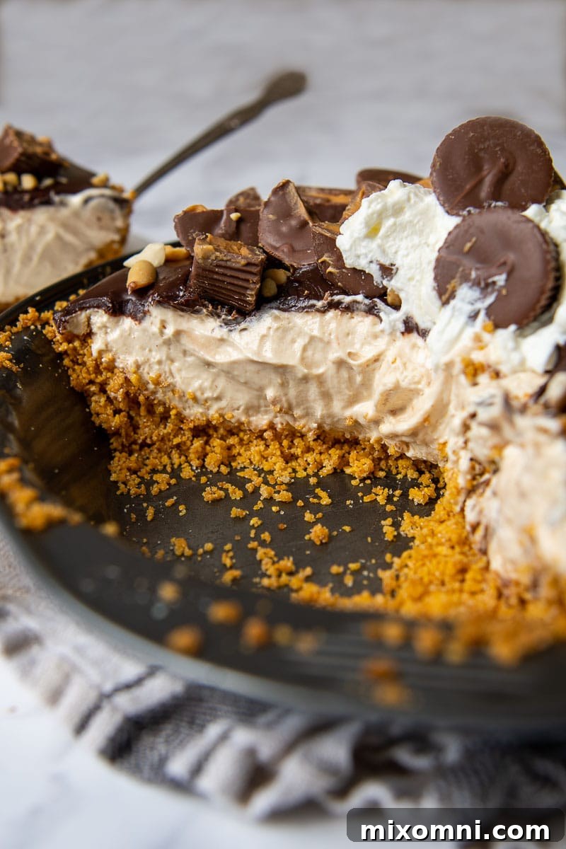 A large slice of chocolate peanut butter pie, garnished with Reese's cups, with a piece removed.