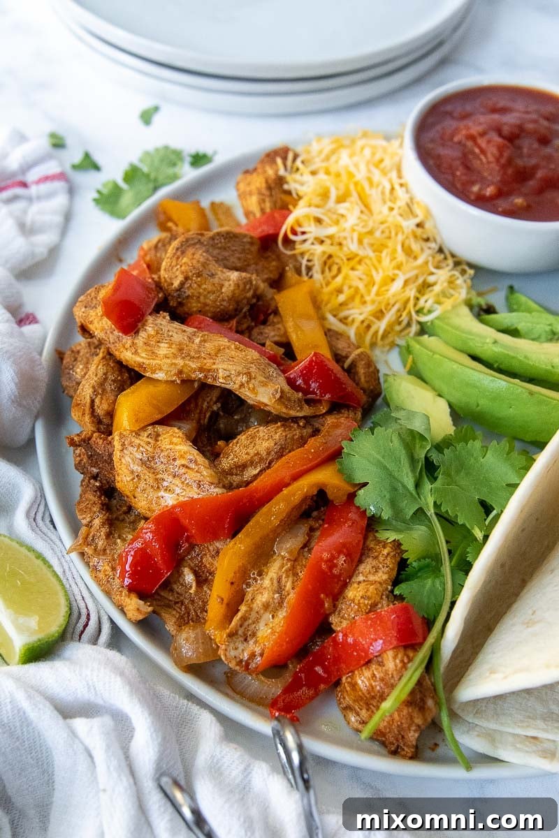 Plate of Instant Pot chicken fajita meat, peppers, and onions with a side bowl of salsa, ready to serve.