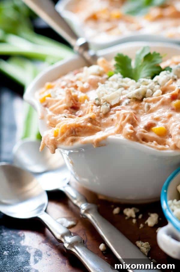 A close-up shot of a rich, creamy buffalo chicken chili served in a rustic bowl with two spoons resting nearby, inviting you to dive in.